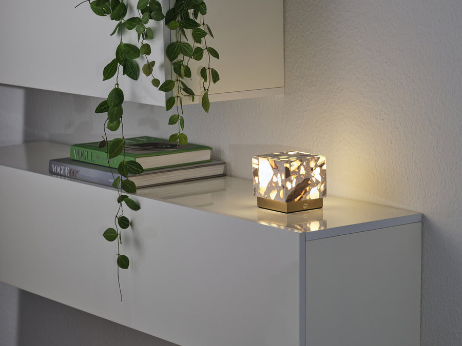 Vue similaire de la lampe éclairée sur le meuble blanc, entourée de végétation et de magazines.