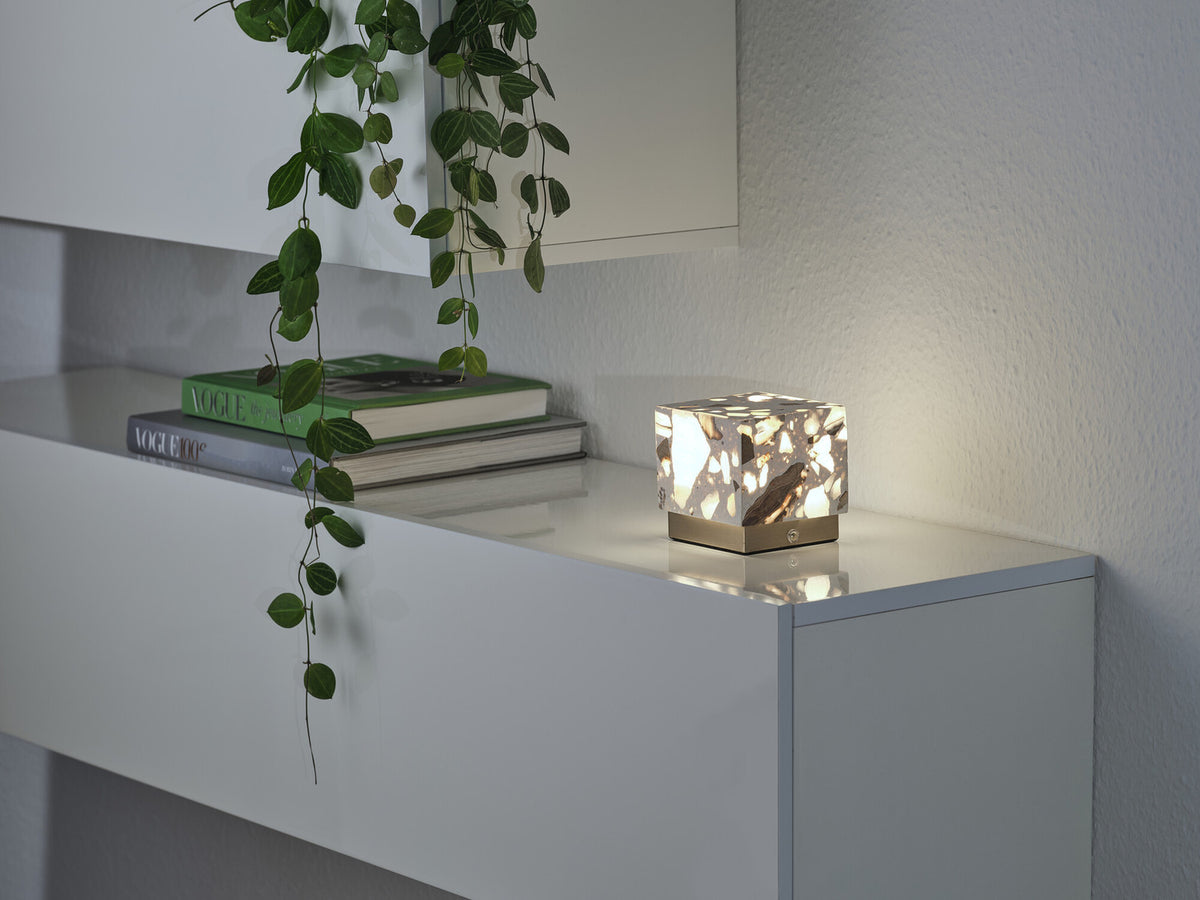 Scène répétée du luminaire allumé sur l'étagère, avec livres empilés et plante retombante.