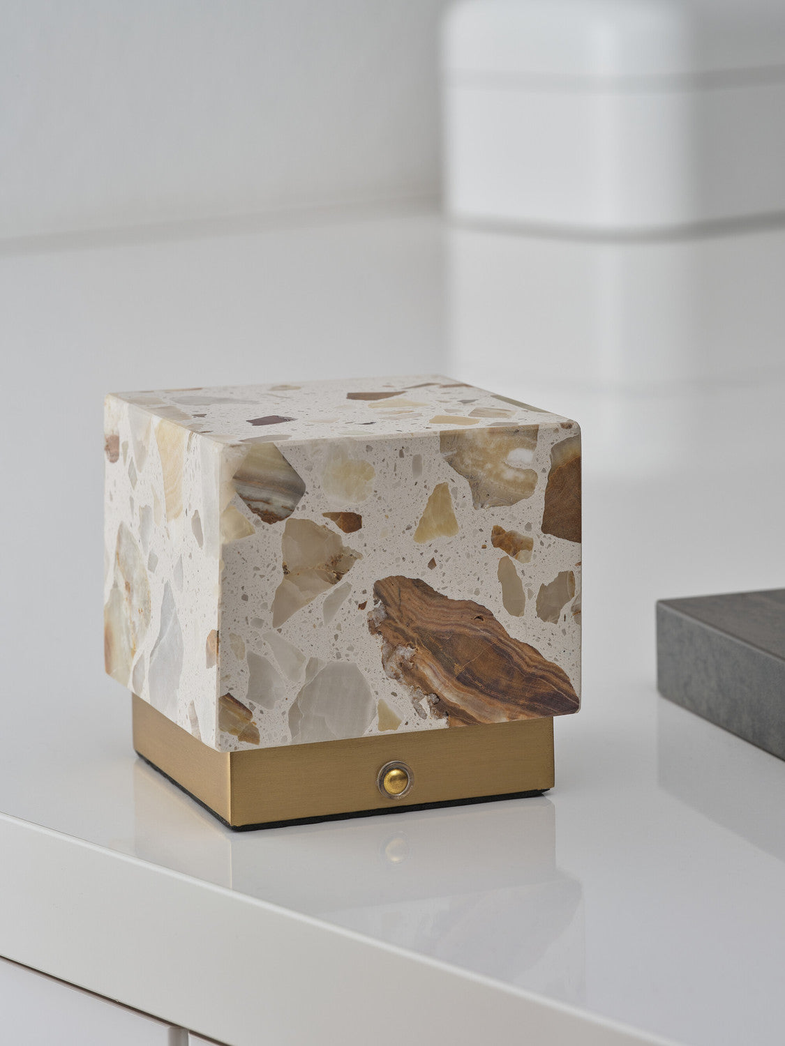 Gros plan du cube terrazzo éteint, posé sur surface brillante, base dorée et bouton.