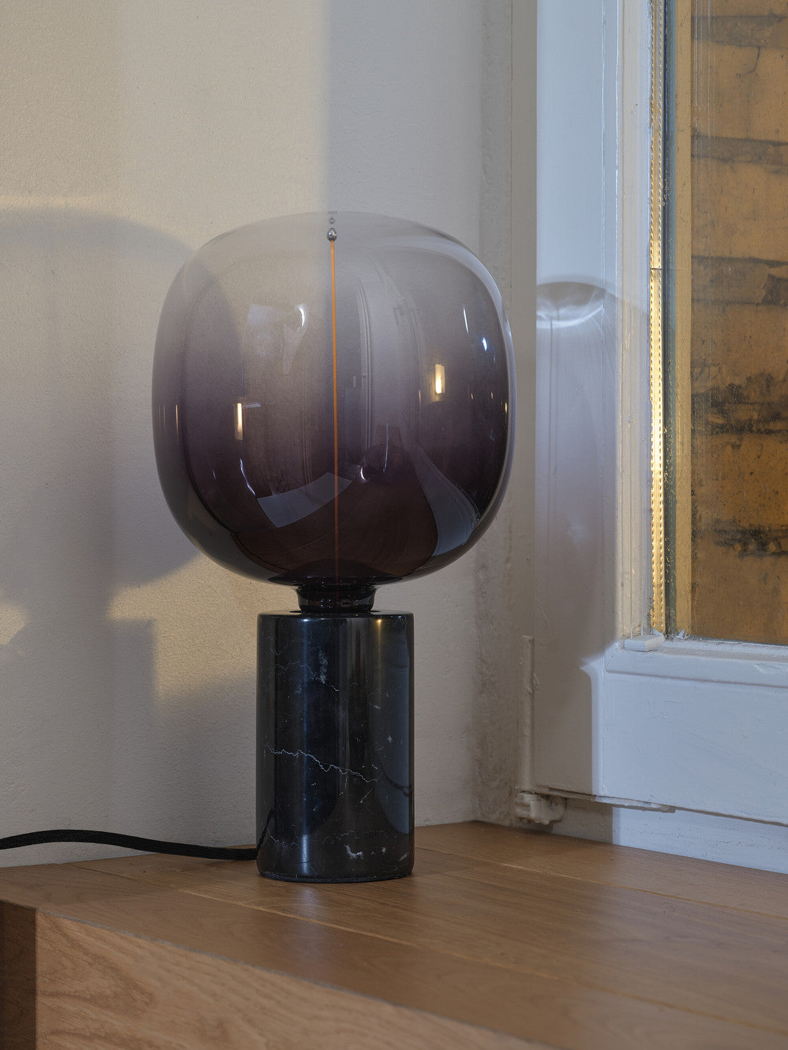 Lampe à poser éteinte sur table en bois, grosse ampoule sphérique fumée et base noire.