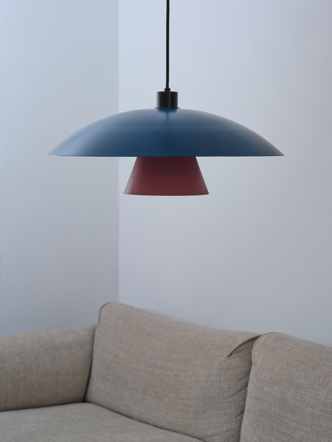 Gros plan de l'abat-jour bleu et du cône fuchsia au-dessus d'un canapé clair.