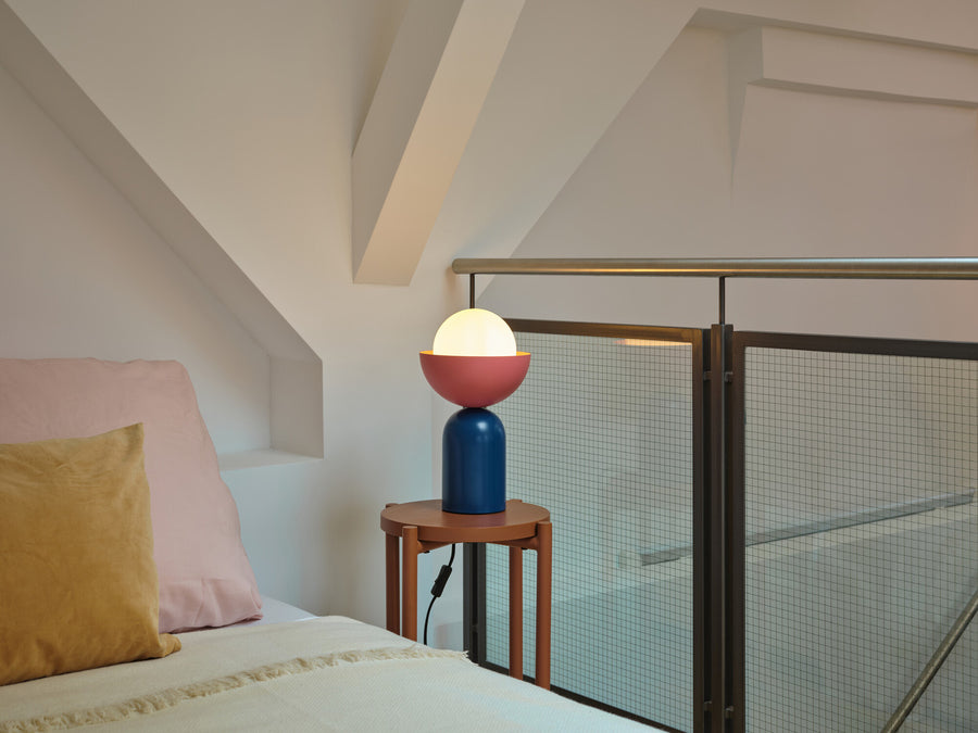 Lampe allumée posée sur une table d'appoint près d'un lit et d'une rambarde.