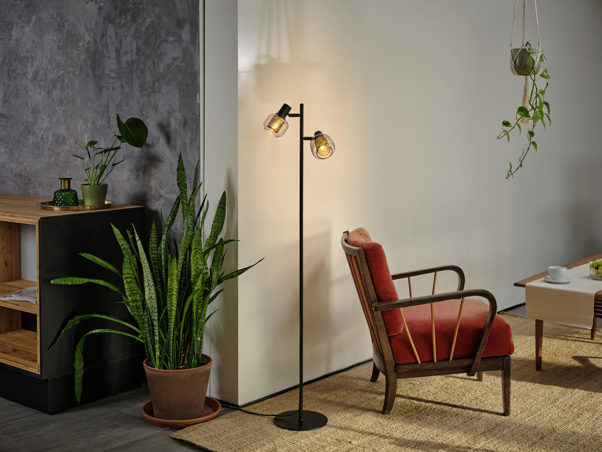 Lampadaire allumé dans un salon, près d'un fauteuil rouge et d'une plante verte.