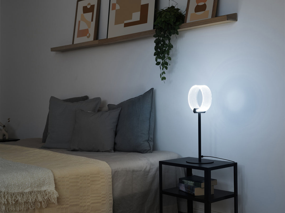 Lampe à poser éclairée sur une table de chevet dans une chambre, ambiance nuit.