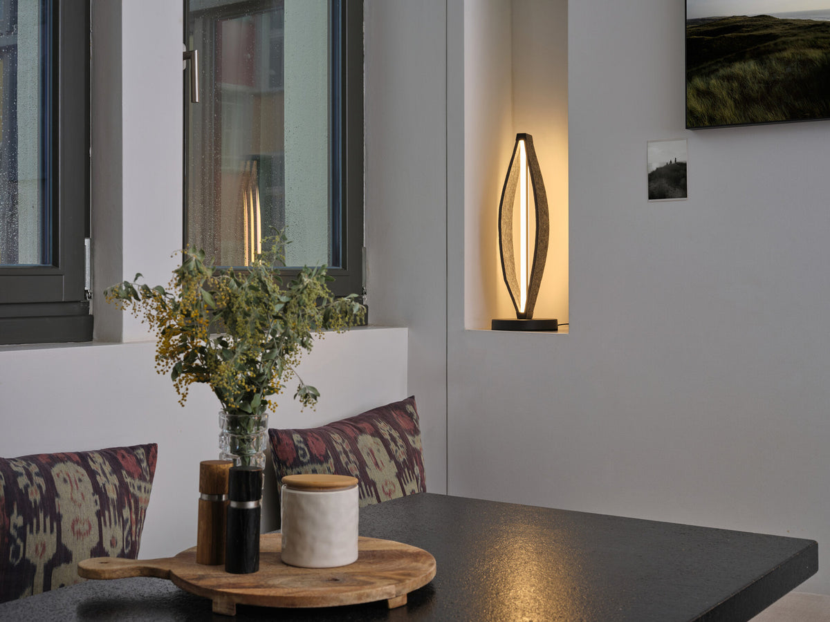Mise en ambiance dans une niche murale, lampe allumée près d'une table et de coussins.