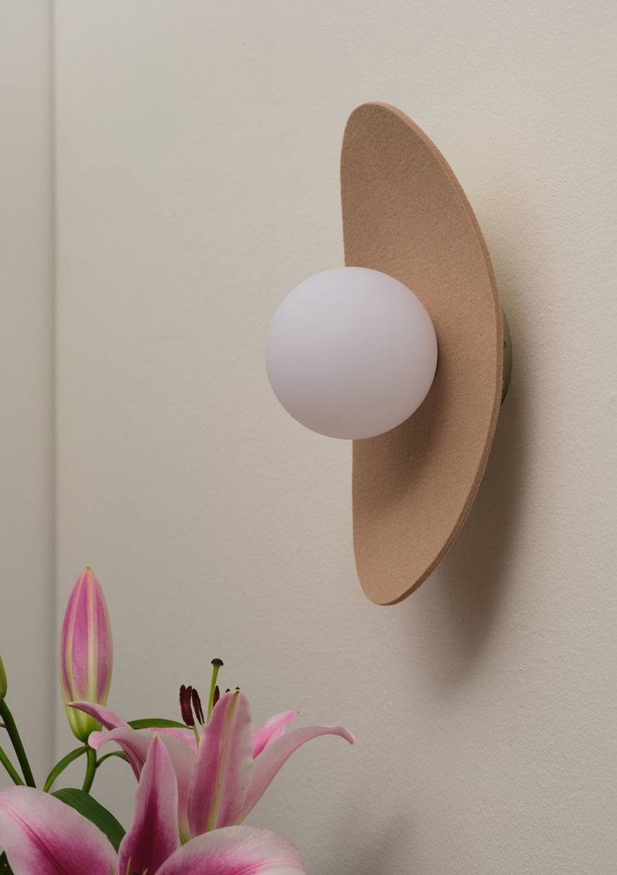 Vue rapprochée de l’applique ovale beige et de son globe blanc devant des lys.