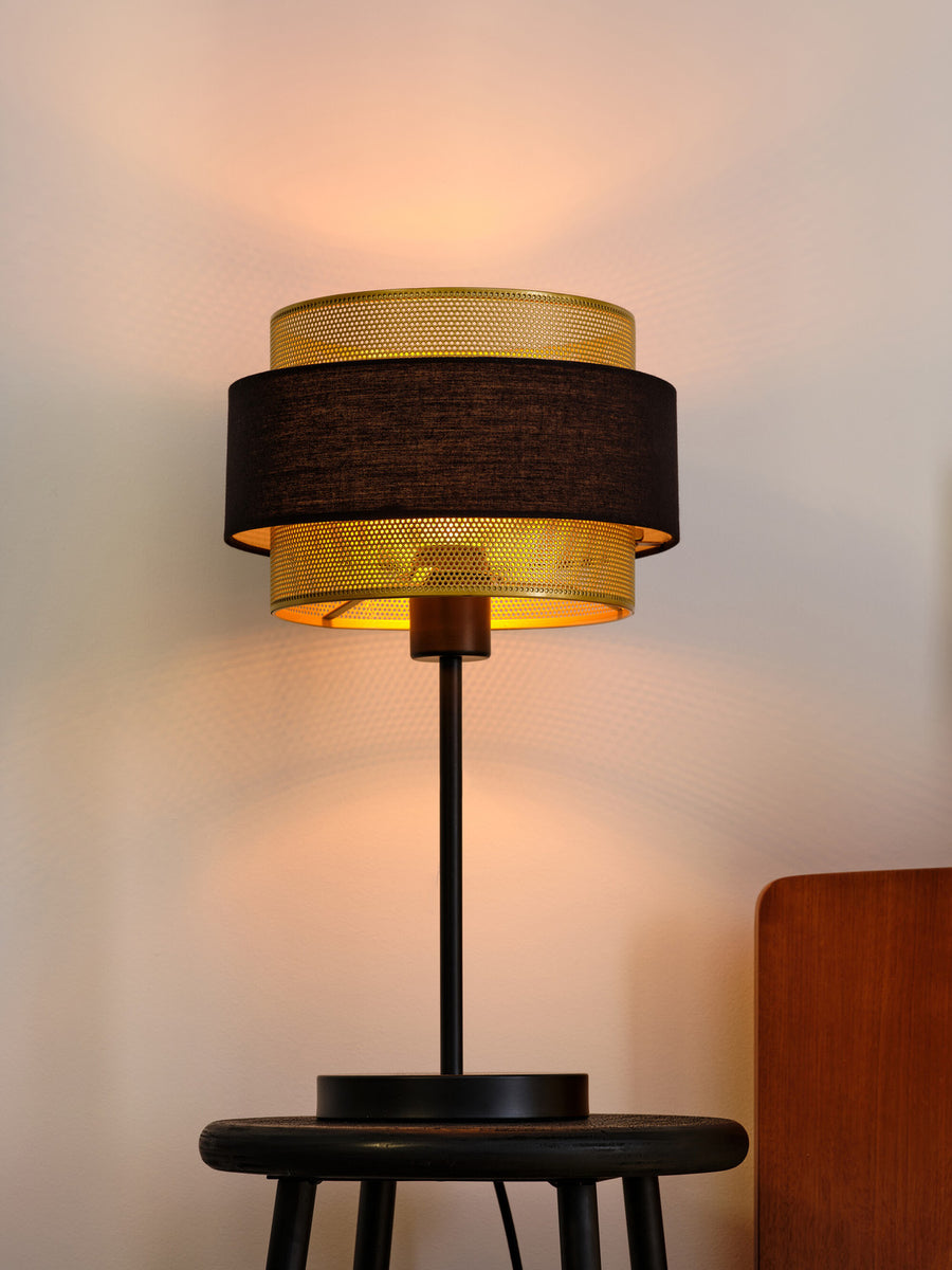 Lampe à poser éclairant un mur blanc, posée sur une table en bois