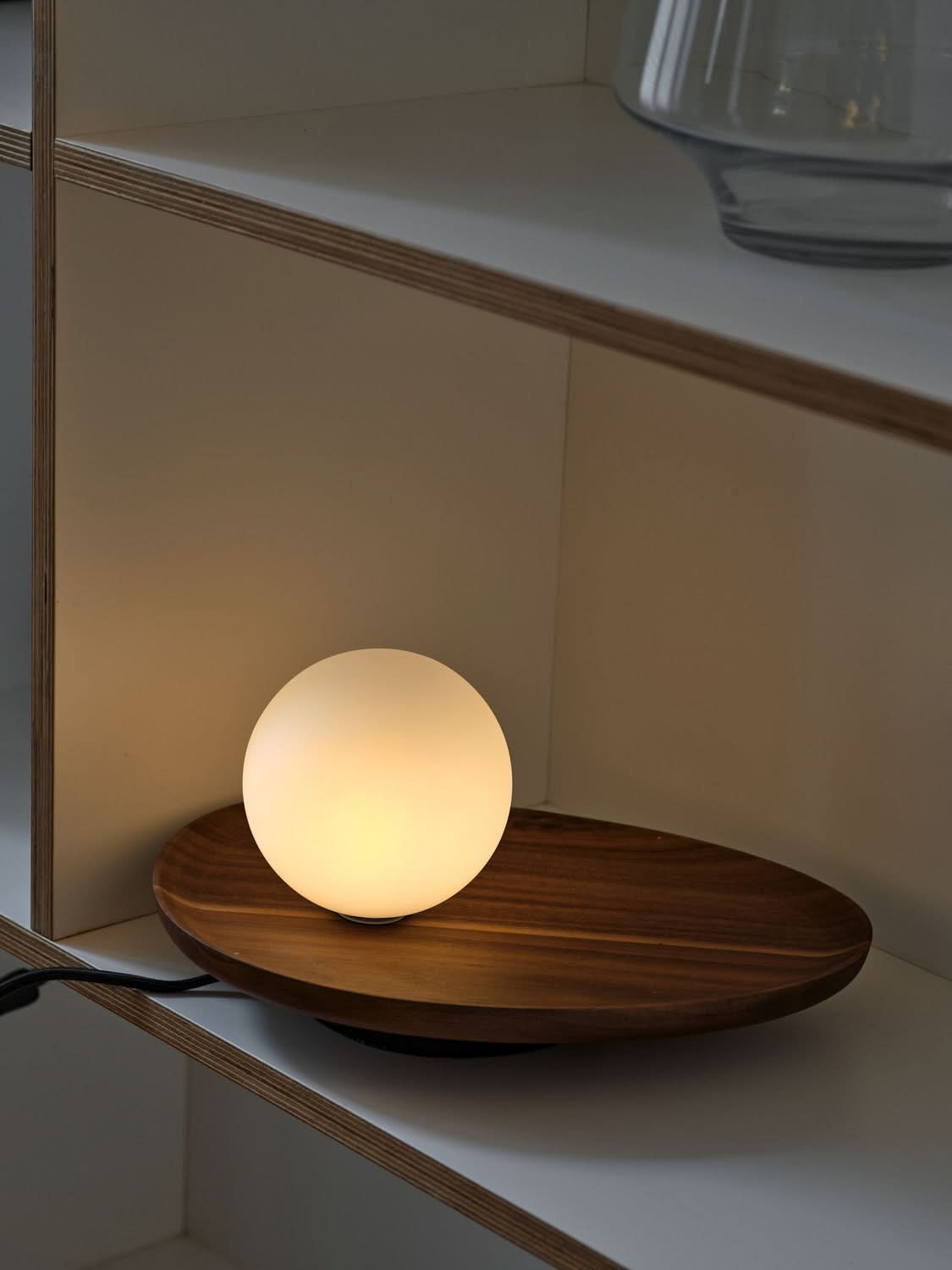 Lampe allumée dans une étagère en bois clair, diffusant une lumière chaude.