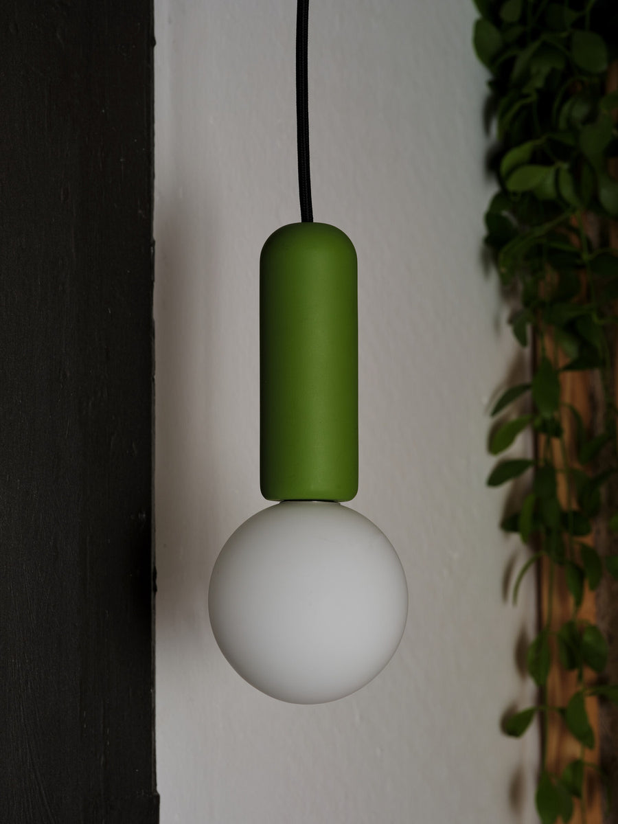 Détail rapproché du cylindre vert en béton et du globe blanc éteint.