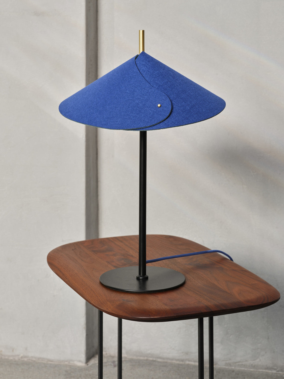 Gros plan de la lampe sur table en noyer, câble bleu et pied noir.