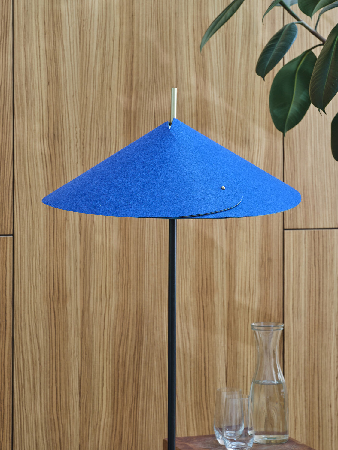 Gros plan sur l'abat-jour conique bleu et la tige fine noire du lampadaire.