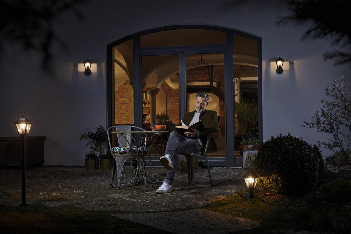 Mise en ambiance nocturne sur une terrasse, homme lisant près de luminaires allumés.