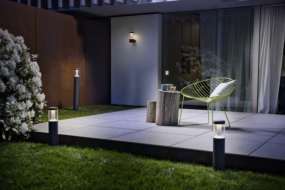 Vue nocturne d'une terrasse avec luminaire mural allumé fixé sur un mur blanc.