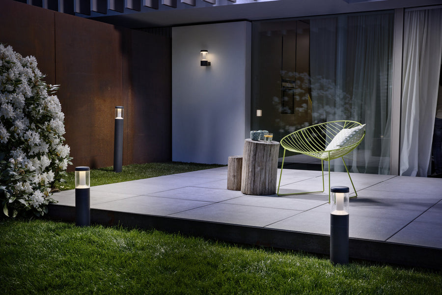 Vue nocturne d'une terrasse avec luminaire mural allumé fixé sur un mur blanc.