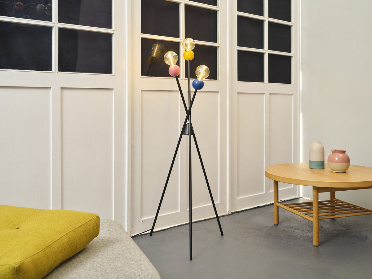 Lampadaire trépied allumé devant portes blanches, près d'une table basse avec vases.