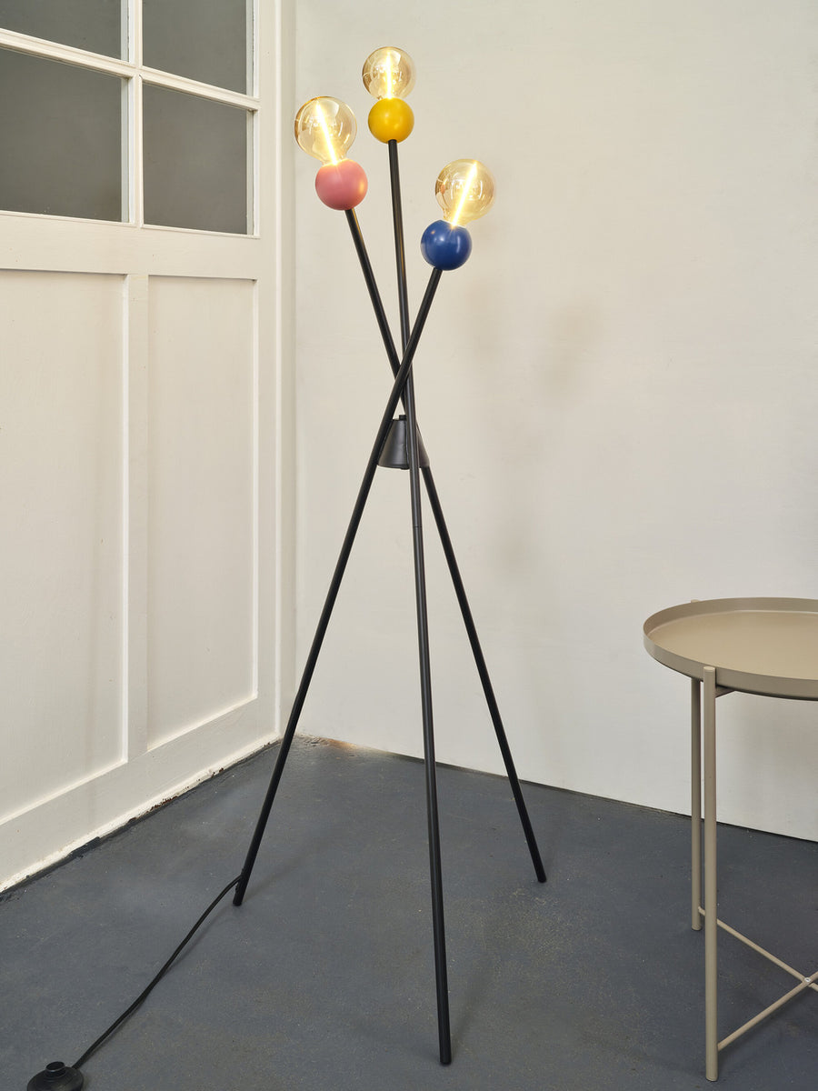 Vue en situation du lampadaire noir allumé, câble au sol et table d'appoint beige.