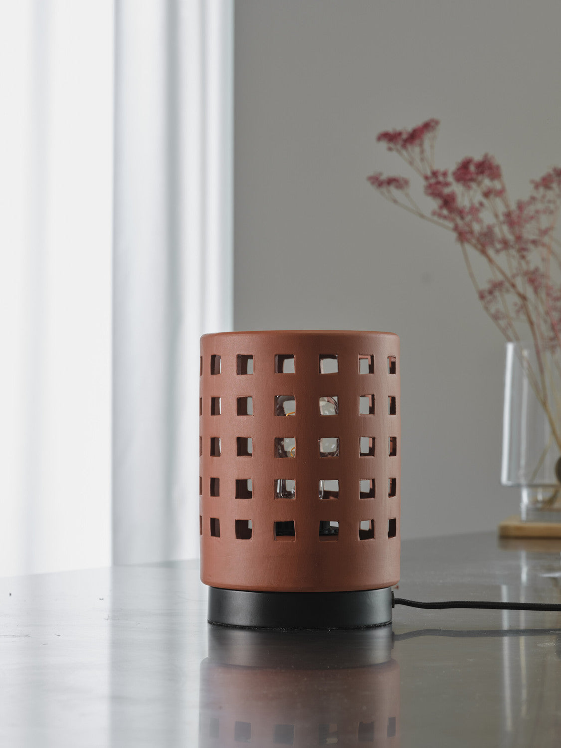 Vue de profil de la lampe éteinte sur une table, câble et vase en arrière-plan.