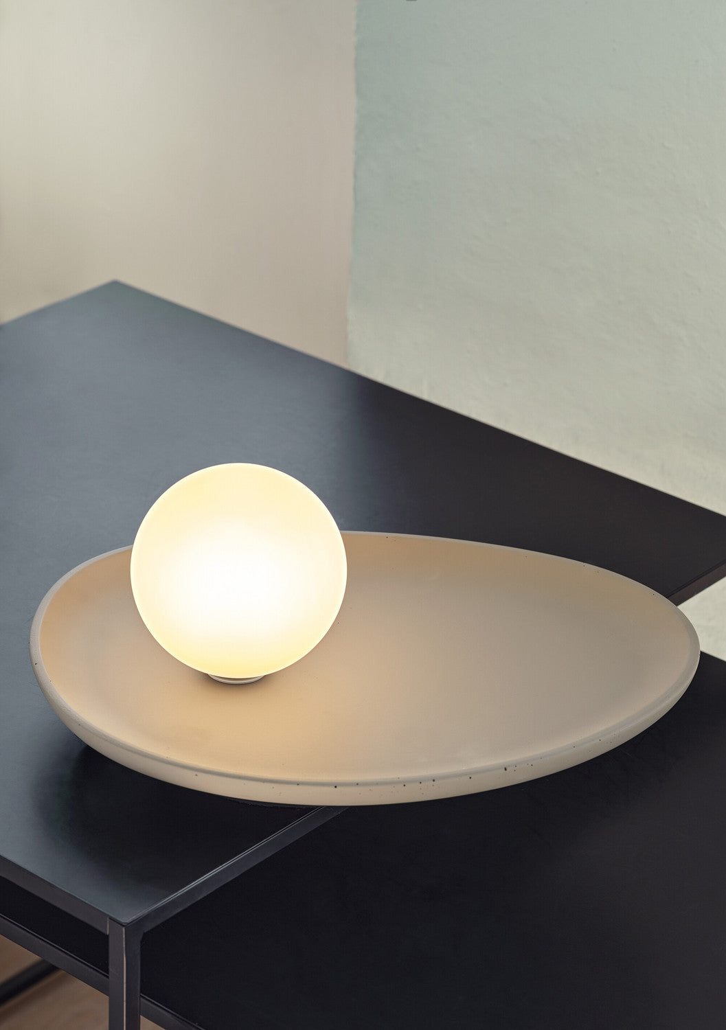 Gros plan d'une lampe allumée sur table bleu foncé, socle beige et globe lumineux.