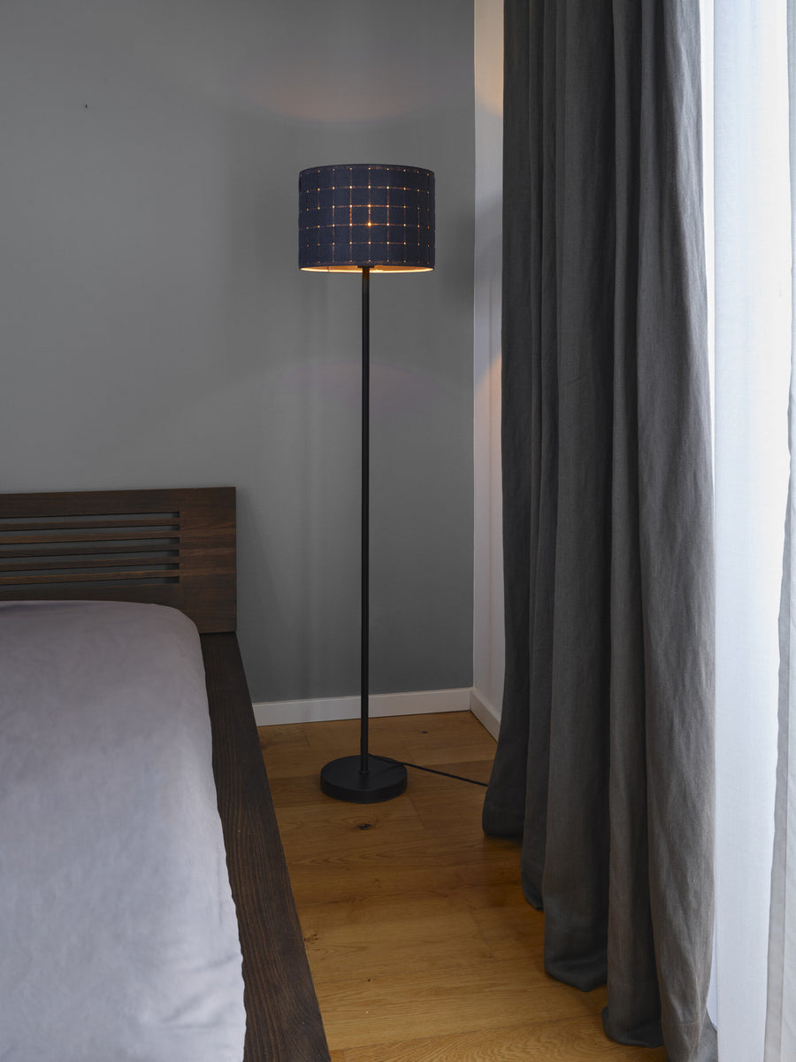 Lampadaire allumé près d'un lit en bois, contre un mur gris et des rideaux.