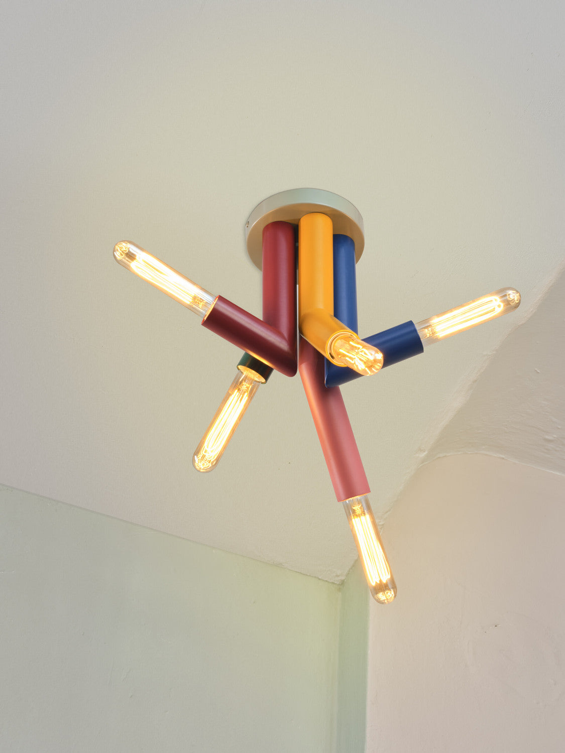 Vue en contre-plongée des tubes colorés et des ampoules filament allumées au plafond.