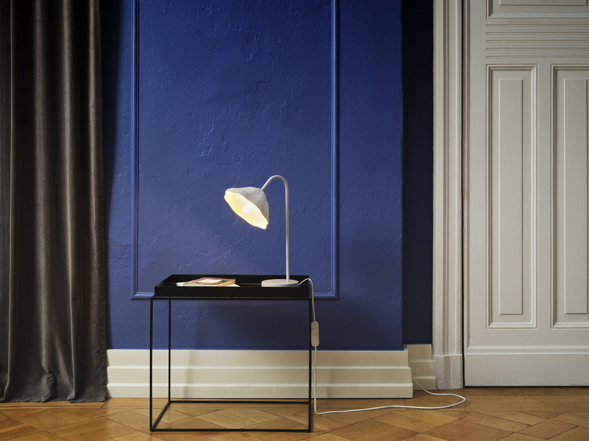 Mise en ambiance : lampe allumée sur une table noire devant un mur bleu profond.