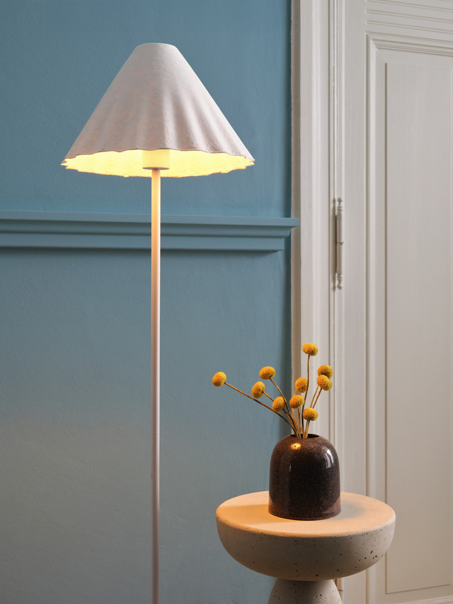 Gros plan sur l'abat-jour conique allumé et un vase à fleurs séchées.