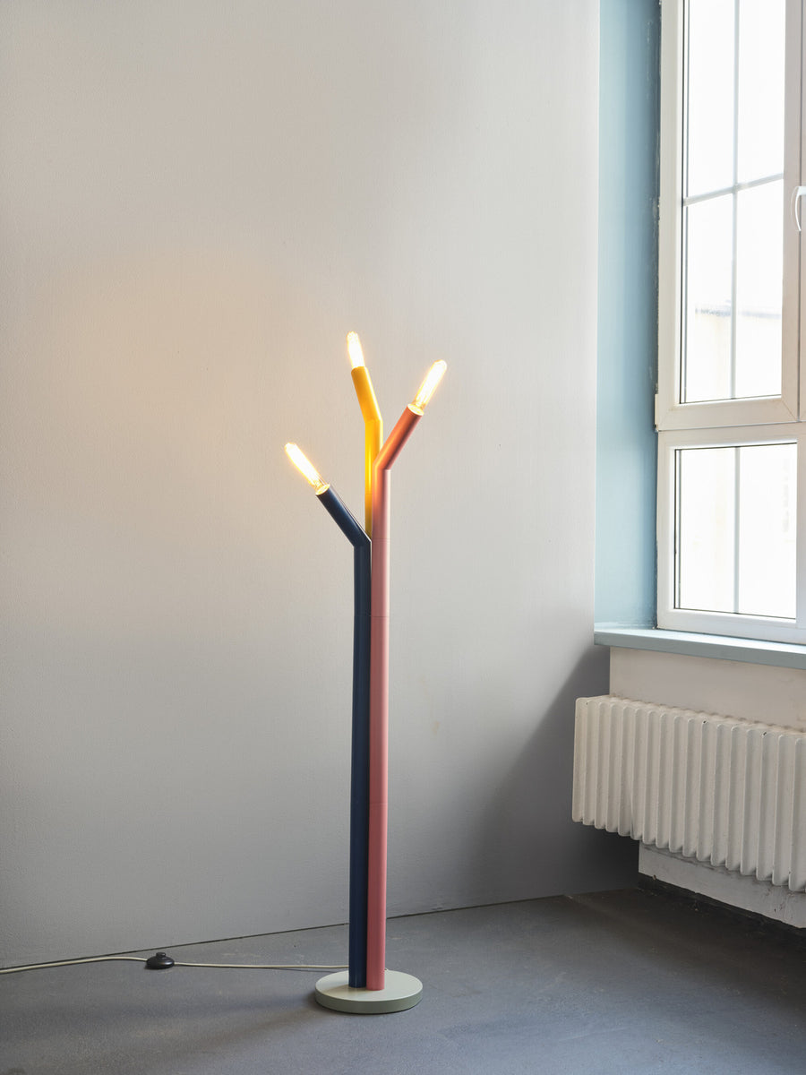 Lampadaire multicolore allumé près d'une fenêtre et d'un radiateur blanc dans une pièce vide.