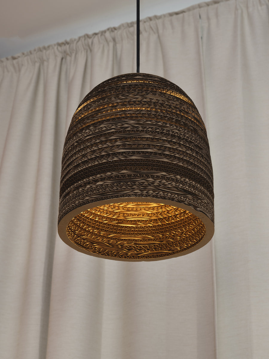 Détail rapproché de l'abat-jour allumé, lumière chaude sur fond de rideau clair.