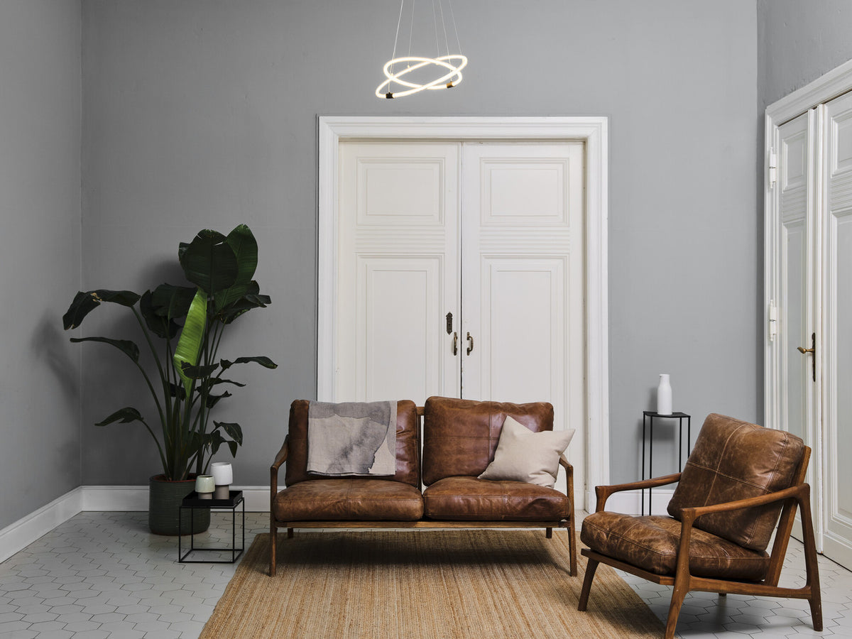 Suspension allumée au-dessus d'un salon gris avec canapé en cuir et plante.