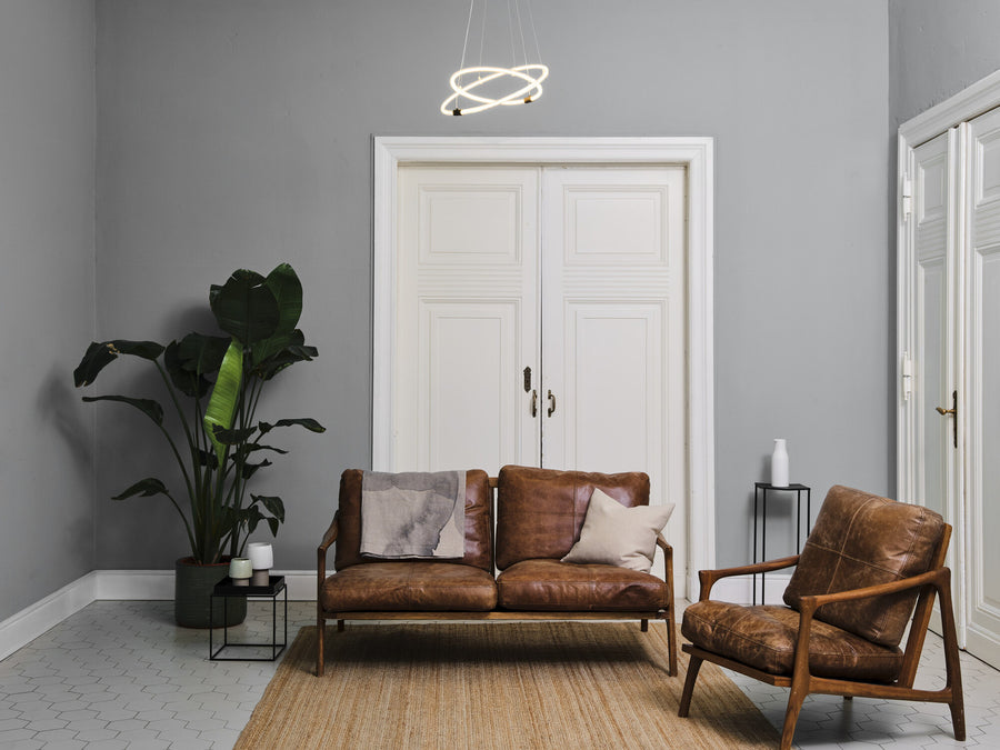 Suspension allumée au-dessus d'un salon gris avec canapé en cuir et plante.