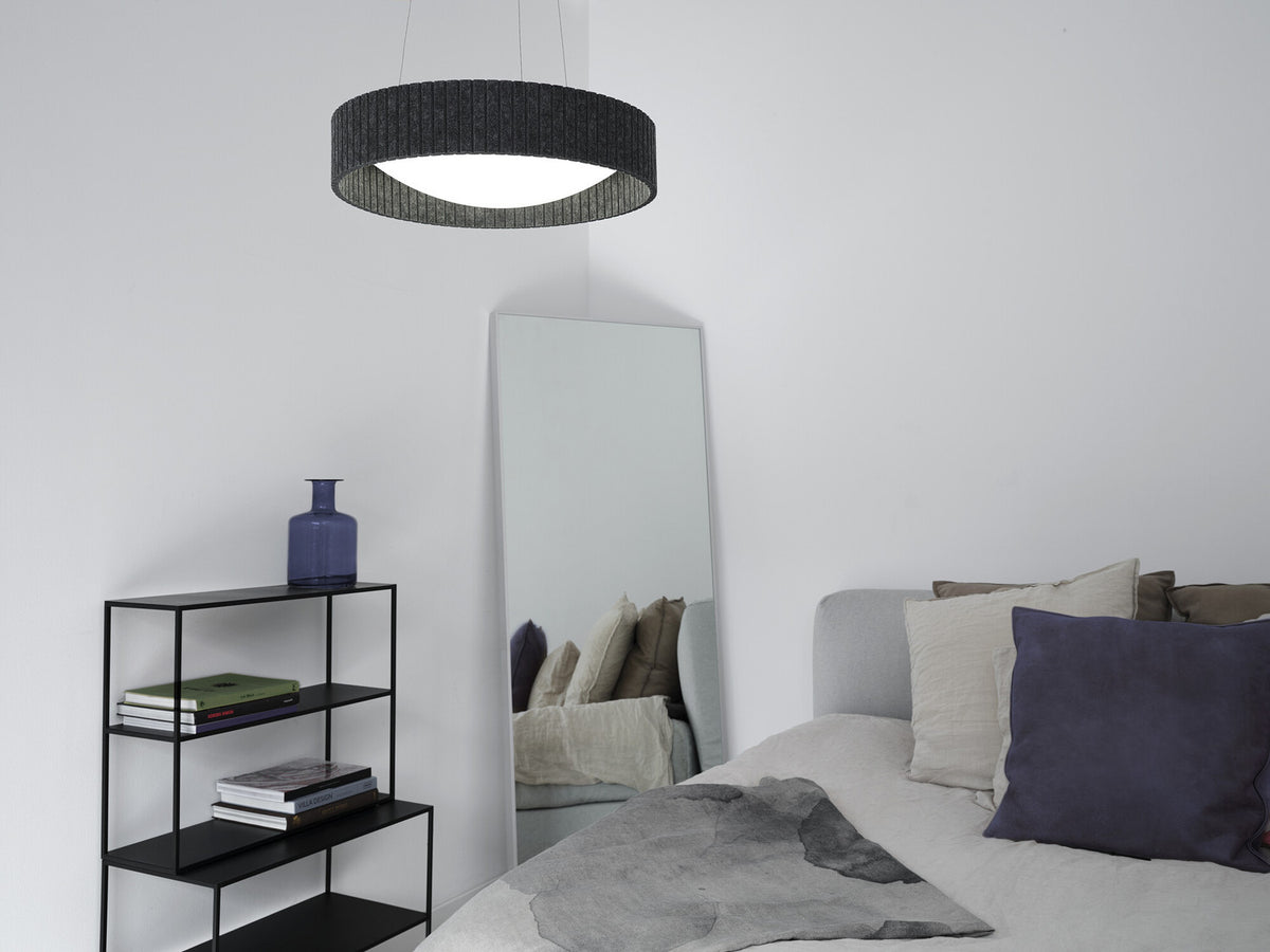 Suspension cylindrique allumée dans une chambre, près d’un miroir et d’une étagère.
