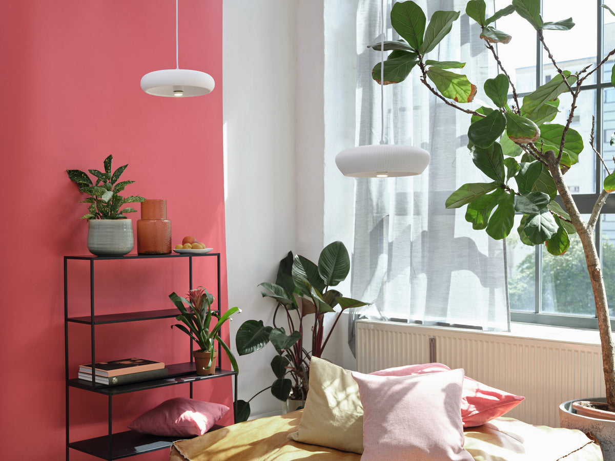 Deux suspensions blanches dans une chambre rose avec lit, coussins et plantes.