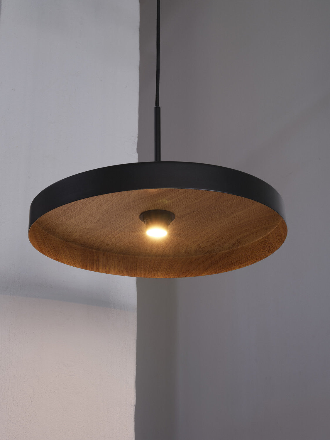 Détail du luminaire allumé : rebord noir et diffuseur en bois éclairé.