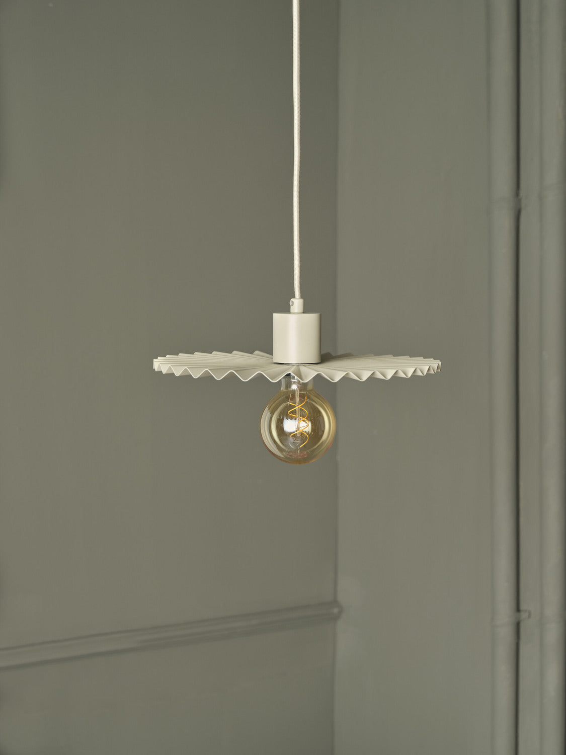 Gros plan sur suspension beige allumée, ampoule globe et abat-jour plissé.
