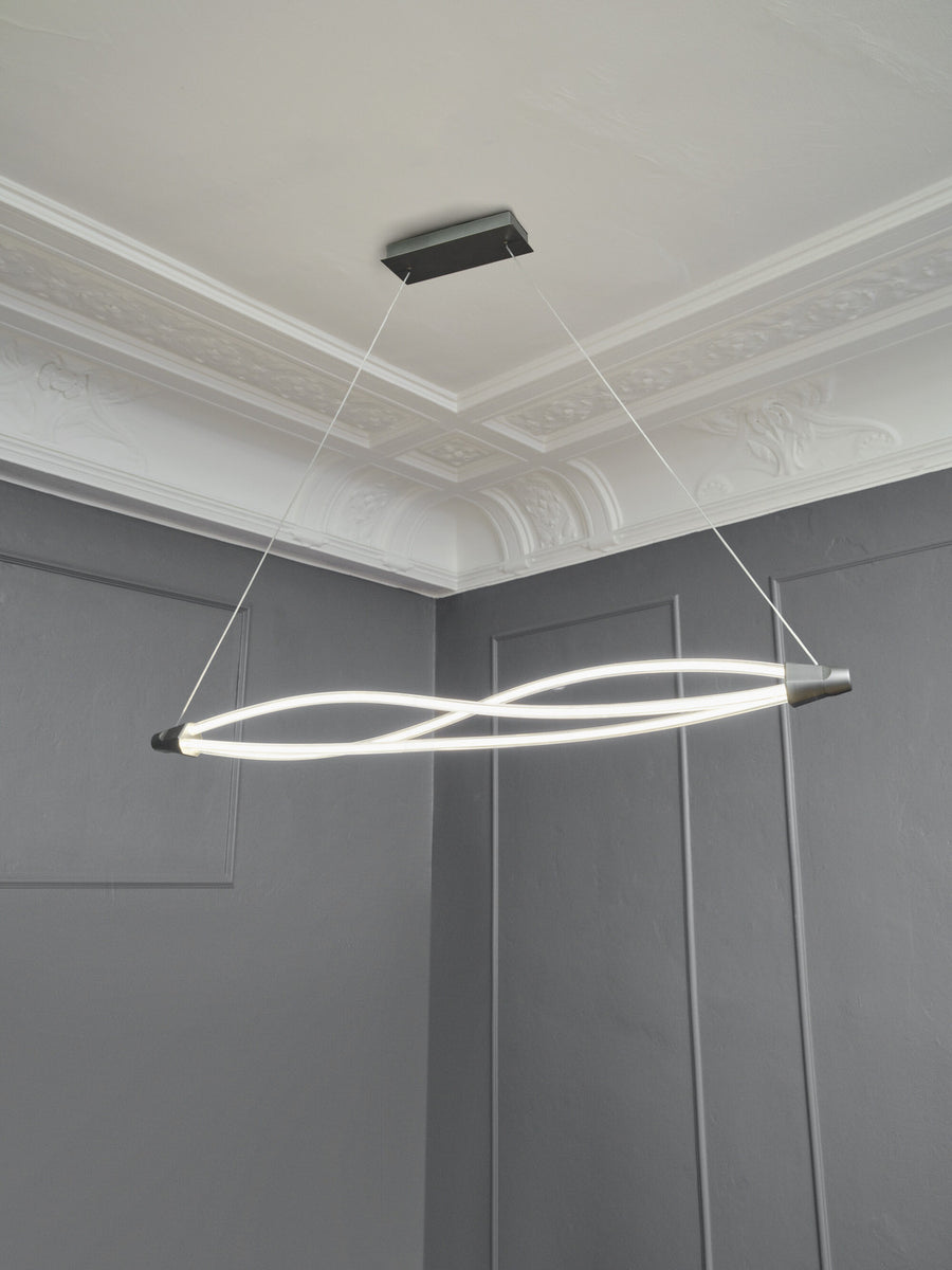 Vue en intérieur de la suspension allumée sous moulures, câbles et fixation plafond visibles.