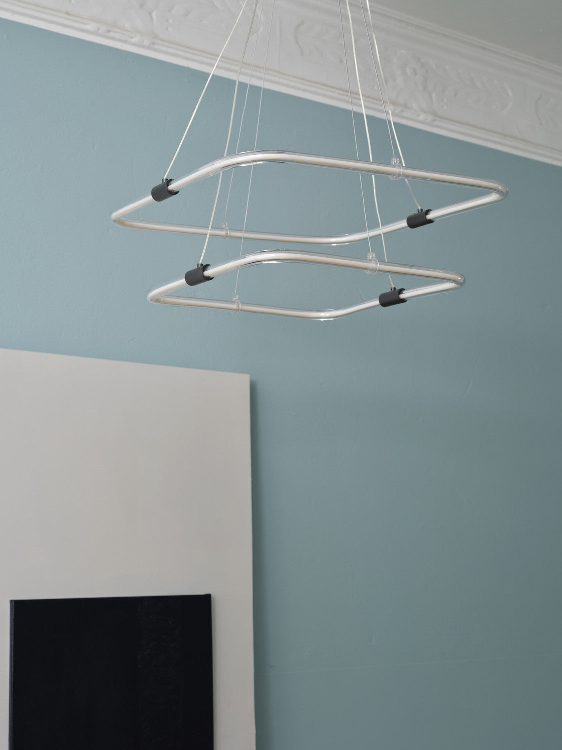 Détail des anneaux lumineux suspendus devant un mur bleu gris.