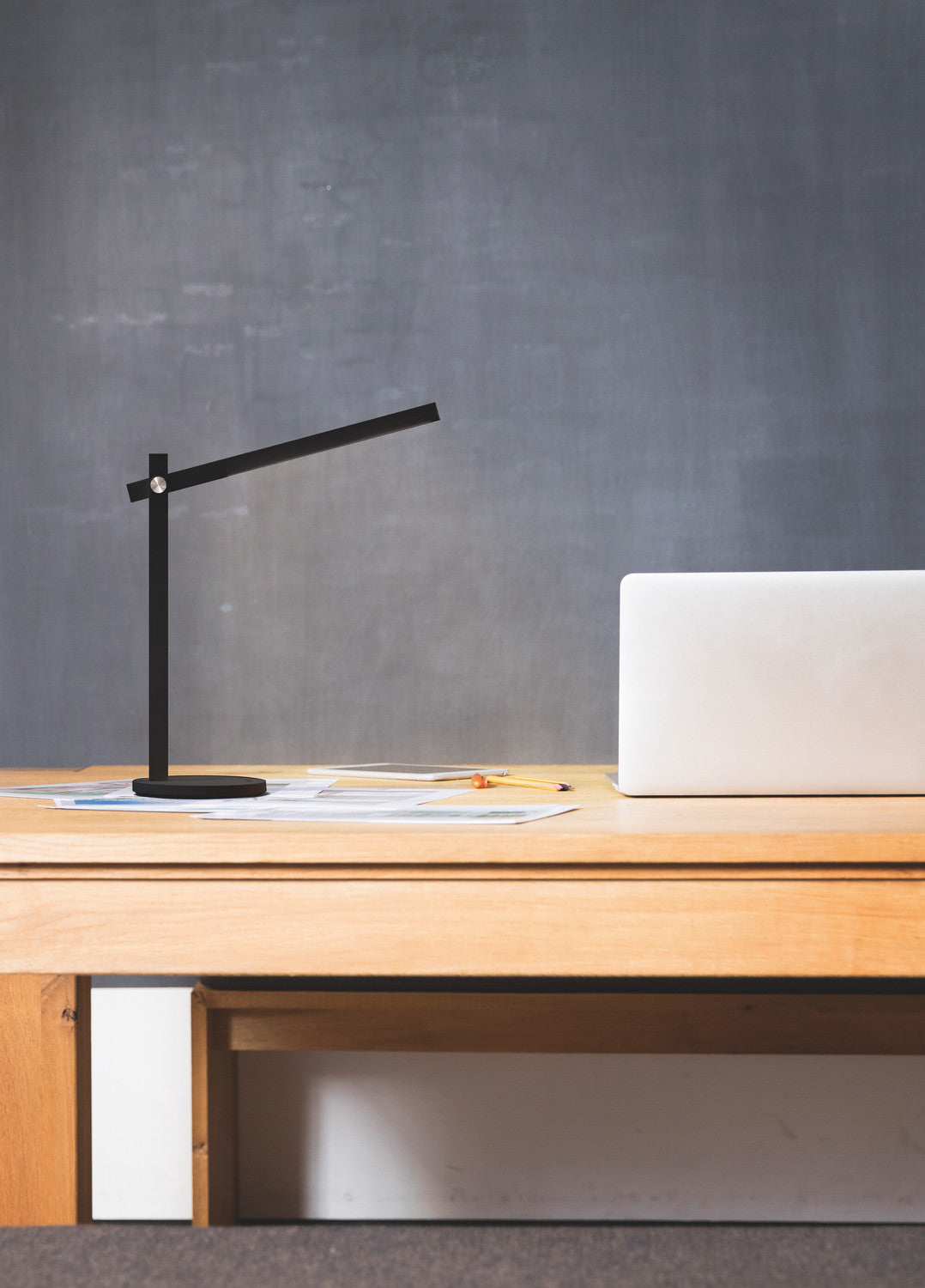 Mise en ambiance de la lampe sur un bureau en bois clair devant un mur gris