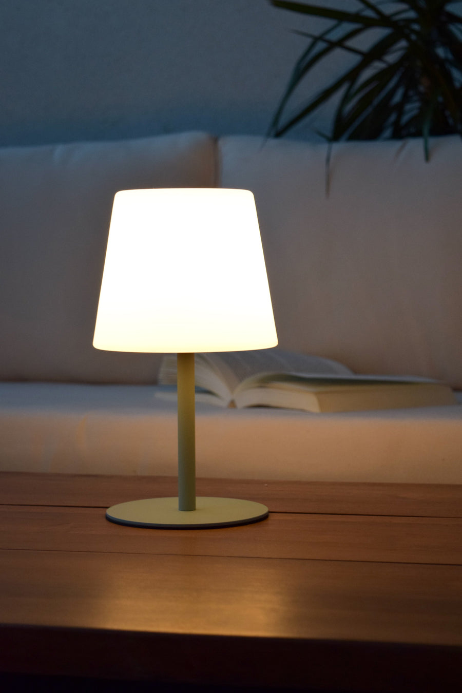 Détail du socle rond vert sauge posé sur une table en bois, lumière chaude
