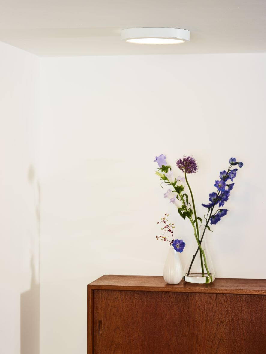 Plafonnier rond blanc fixé au plafond dans un intérieur épuré avec commode en bois