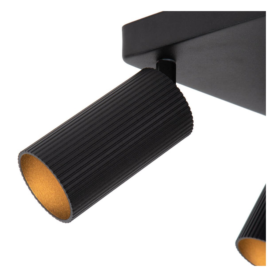 Gros plan sur un projecteur cylindrique noir strié, intérieur doré et fixation orientable.