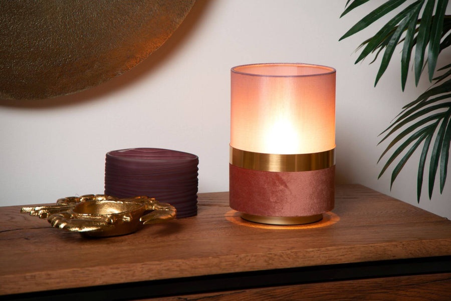 Vue rapprochée de la lampe rose et dorée posée sur un meuble en bois.