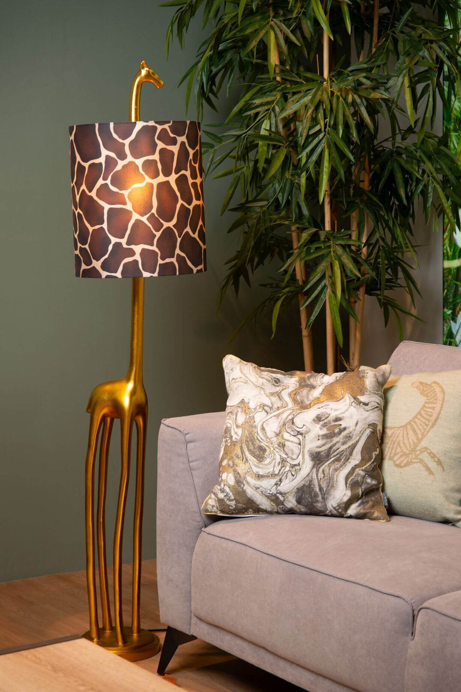 Lampadaire girafe doré installé près d'un bambou et d'un canapé gris.