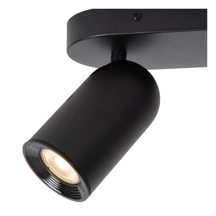 Détail d'un spot cylindrique noir orientable, lentille striée et finition mate sur fond blanc