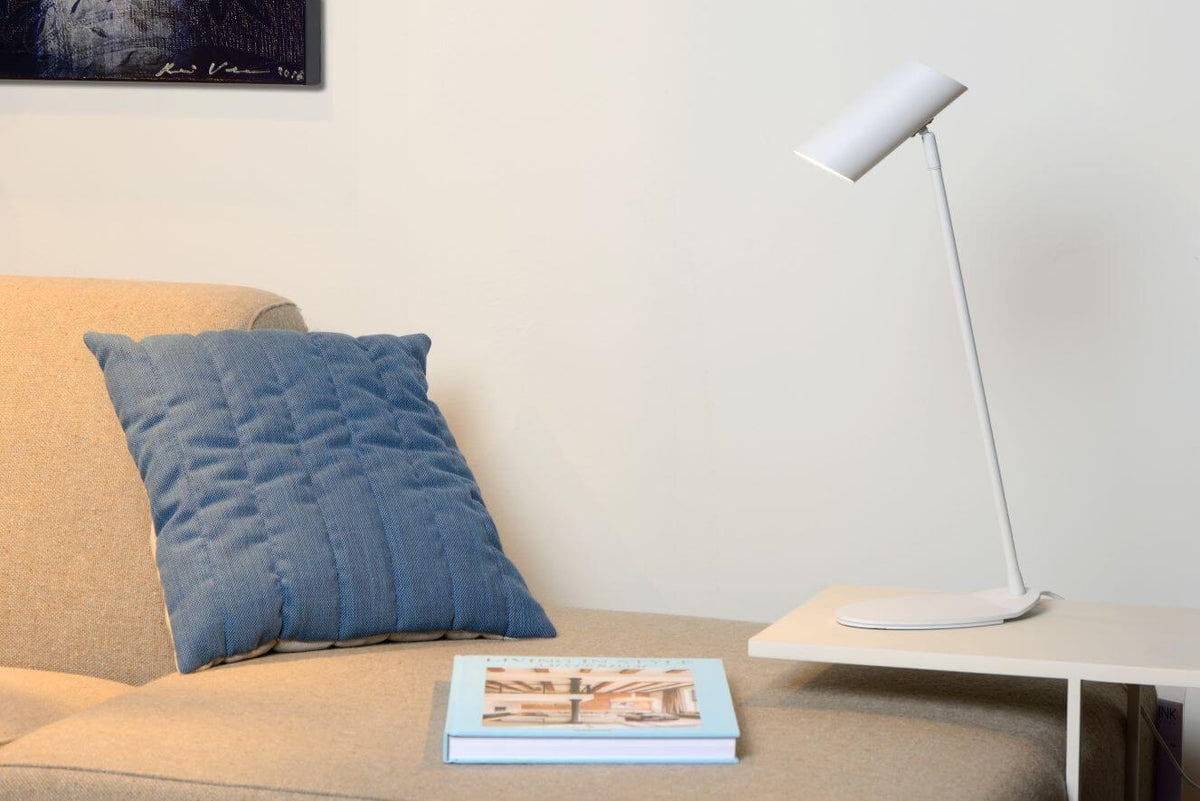 Vue rapprochée du luminaire blanc sur table, avec coussin bleu et livre en décor.