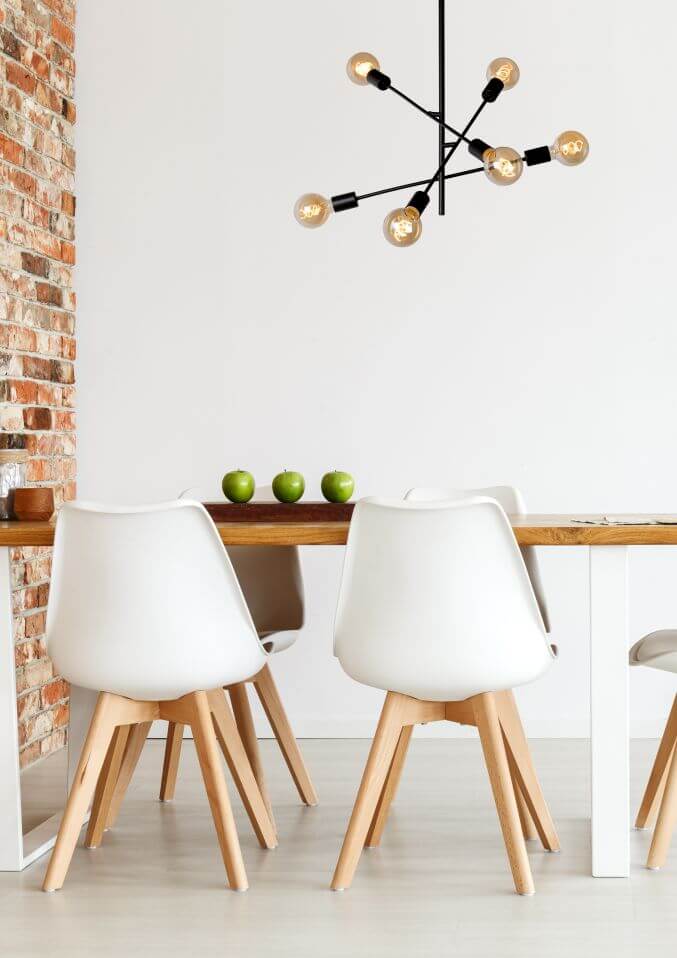 Vue rapprochée du plafonnier allumé, surmontant des chaises blanches et des pommes vertes