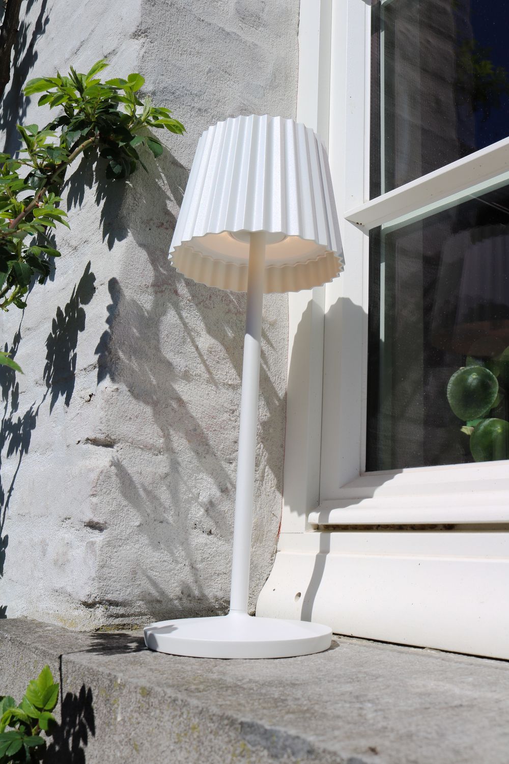 Mise en ambiance extérieure, lampe allumée avec ombres des feuilles sur le mur