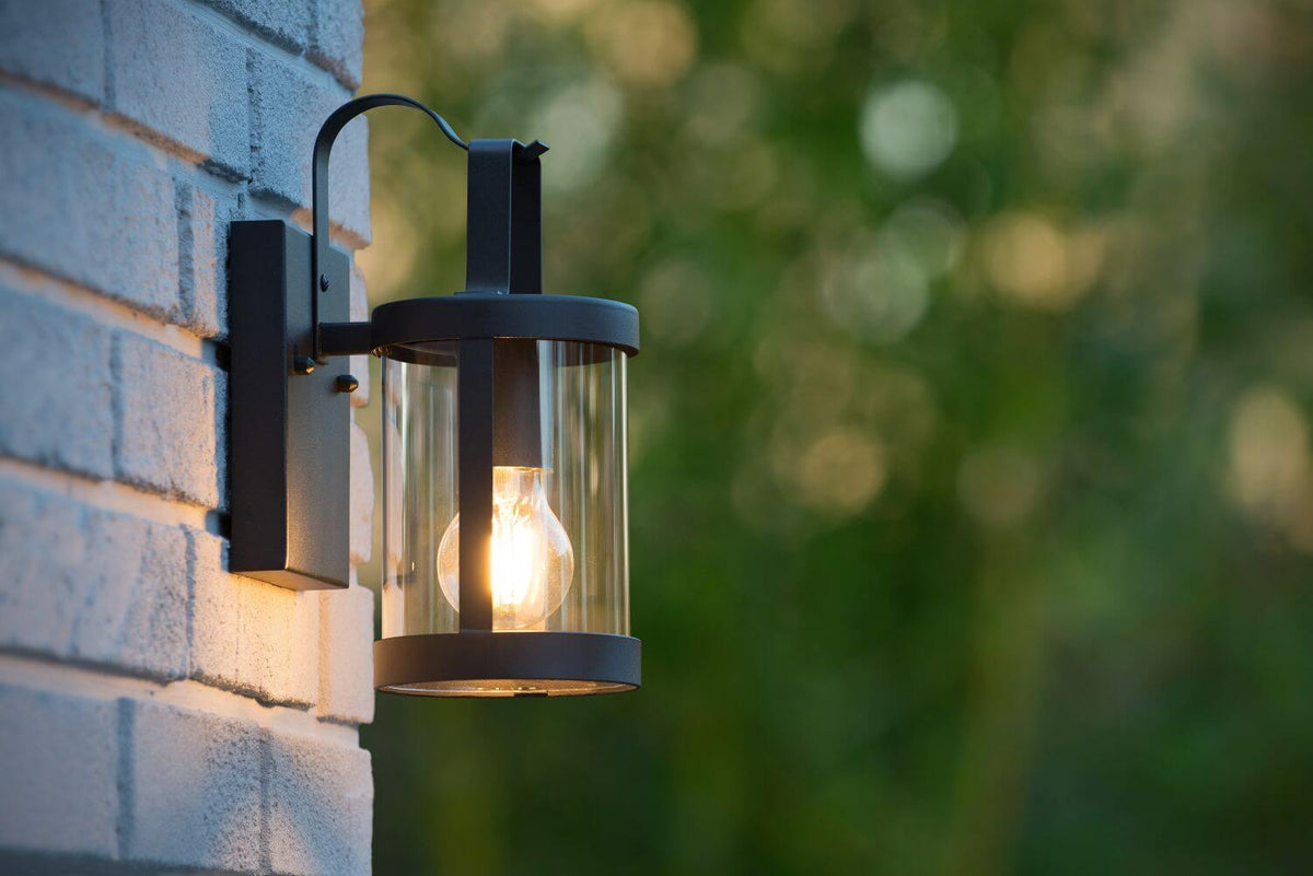Gros plan de l'applique noire avec ampoule Edison allumée, verre cylindrique transparent.
