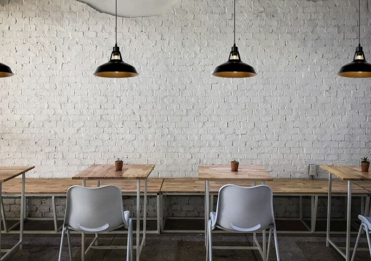 Trois suspensions alignées au-dessus de tables en bois devant un mur de briques blanches
