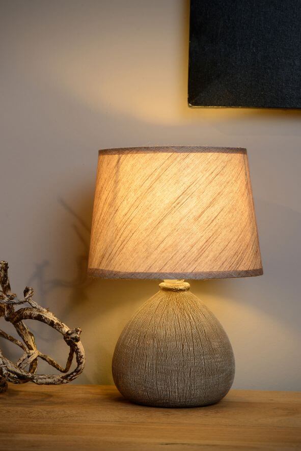 Vue rapprochée de la lampe allumée, abat-jour en coton et base texturée, décor de branches.