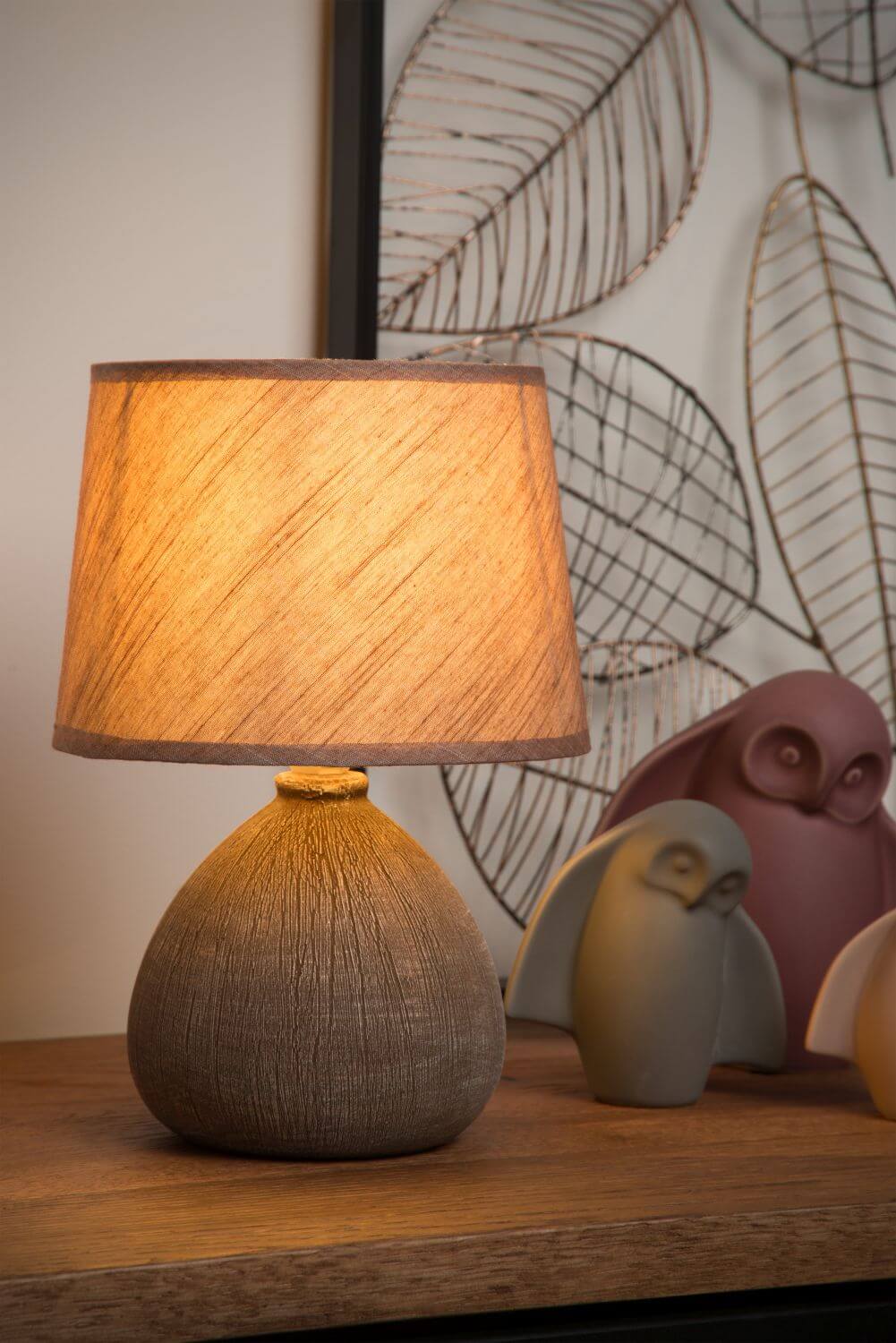 Lampe allumée posée sur un meuble, entourée de chouettes décoratives et de feuillages en métal.